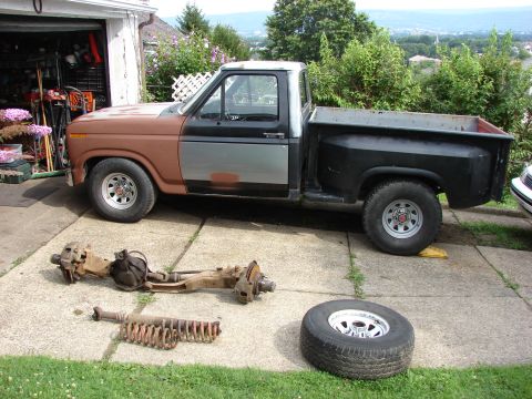1985 Ford F-150 - Ford F-150 pickup truck with front suspension components and a spare tire removed and placed on the ground.
