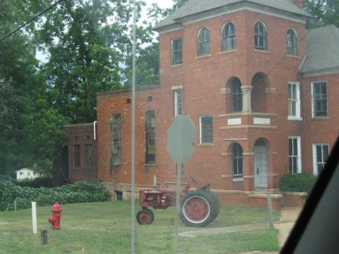 1978 Ford Bronco - A vintage red tractor sits idle on the lawn of an old brick building.