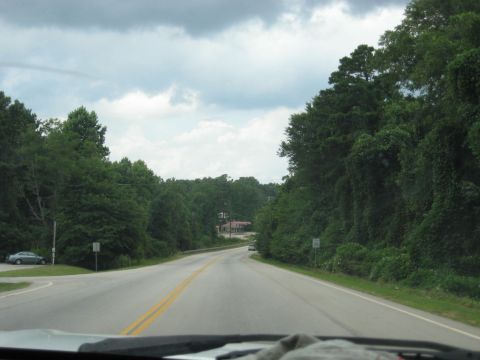 1978 Ford Bronco - Driving down a rural road surrounded by dense trees under a cloudy sky.