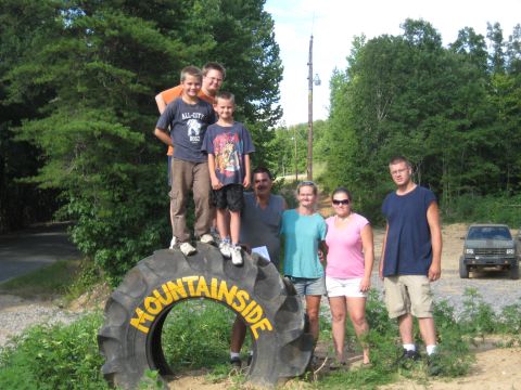 1978 Ford Bronco - Group poses on a large tire with 'MOUNTAINSIDE' text. A truck is in the background.