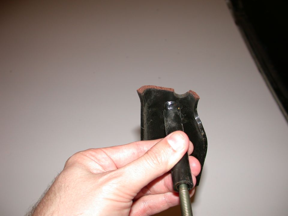 Hand holding a black automotive part with a metal threaded rod