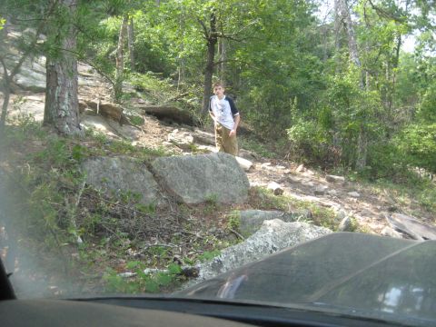 1978 Ford Bronco - A person stands on a rocky, wooded trail, viewed from the perspective of a vehicle's interior.