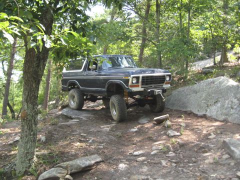 1978 Ford Bronco - A dark blue 1978 Ford Bronco navigates a rocky, wooded terrain.