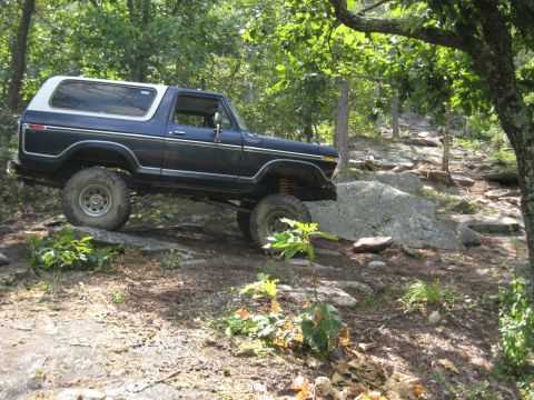 1978 Ford Bronco - 1978 Ford Bronco navigating a challenging rocky path in a wooded area.