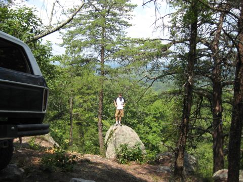 1978 Ford Bronco - A 1978 Ford Bronco is seen from the rear, parked on a dirt path with a person standing on a rock in the background.