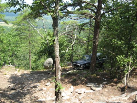 1978 Ford Bronco - A 1978 Ford Bronco is parked on a dirt path surrounded by trees and rocks, with a valley visible in the distance.