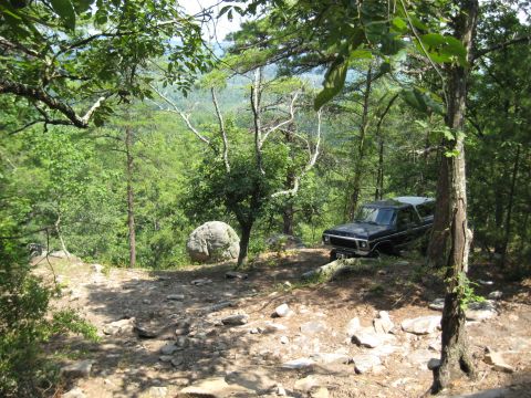 1978 Ford Bronco - A black 1978 Ford Bronco is parked on a dirt path surrounded by trees and rocks, overlooking a valley.