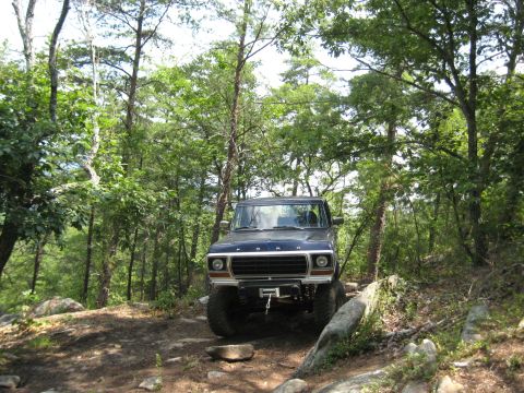 1978 Ford Bronco - Dark blue 1978 Ford Bronco navigating a rough, wooded trail.