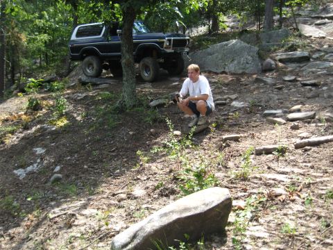 1978 Ford Bronco - A man pauses on a trail next to a classic Ford Bronco, surrounded by trees and large rocks.