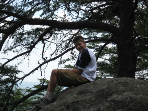 1978 Ford Bronco - A young man enjoys a moment of rest on a large rock, surrounded by the natural beauty of trees and a distant landscape.