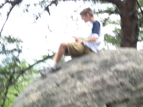 1978 Ford Bronco - A young person sits on a boulder, engrossed in their mobile device amidst a natural setting.