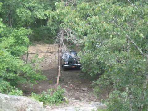 1978 Ford Bronco - A black SUV navigates a challenging off-road trail through a wooded area.