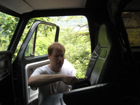 1978 Ford Bronco - A man is seen inside the cab of a truck with the door open, looking out at a wooded landscape.