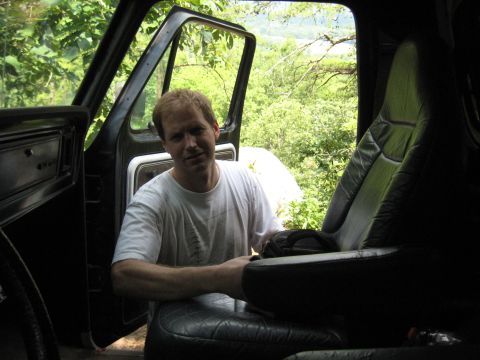 1978 Ford Bronco - Man sits in the driver's seat of a vehicle, with the door open to reveal a scenic outdoor view.