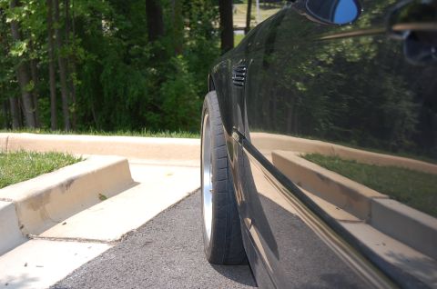 2002 BMW M3 - A close-up side view of a black car's rear wheel and fender, showing vents on the body.