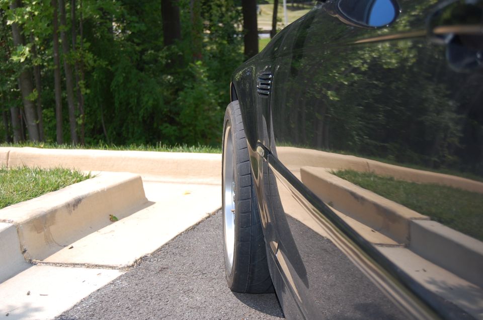 Low side shot of lowered black coupe with cambered front wheel and stretched tire
