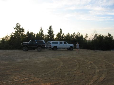 1978 Ford Bronco - A dark blue 1978 Ford Bronco is parked next to a white SUV and a trailer in an open, dusty area with trees in the background.