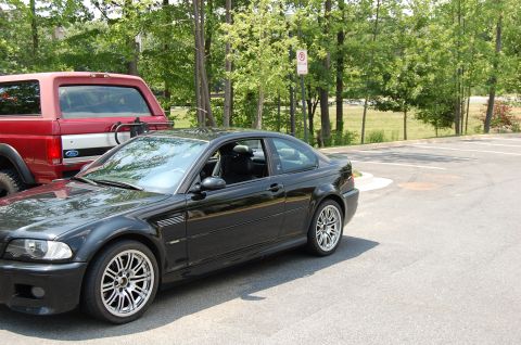 2002 BMW M3 - A black 2002 BMW M3 coupe is parked in a lot next to a red Ford Bronco.