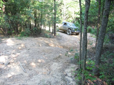 1978 Ford Bronco - A green pickup truck navigates a dirt trail surrounded by trees.