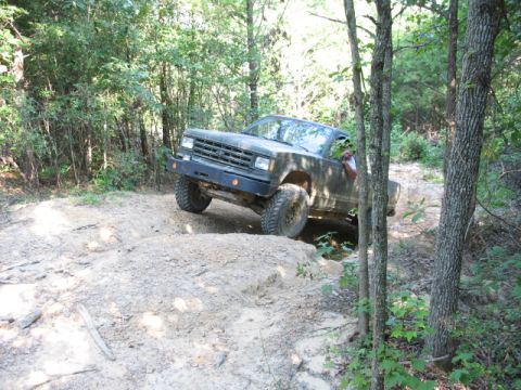 1978 Ford Bronco - A pickup truck navigates a challenging off-road trail surrounded by dense forest foliage.