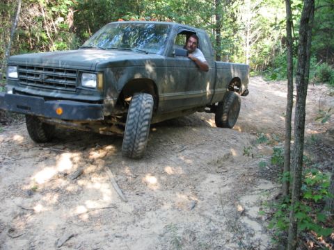 1978 Ford Bronco - A man drives a lifted green pickup truck through a wooded off-road trail.