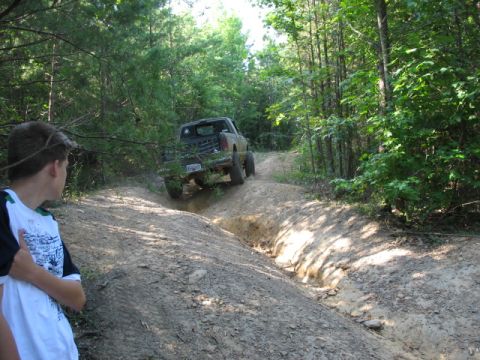 1978 Ford Bronco - A pickup truck navigates a challenging off-road trail surrounded by dense forest.