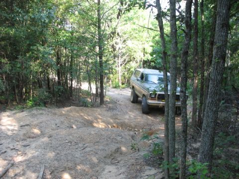 1978 Ford Bronco - 1978 Ford Bronco navigates a rough dirt path surrounded by dense forest.