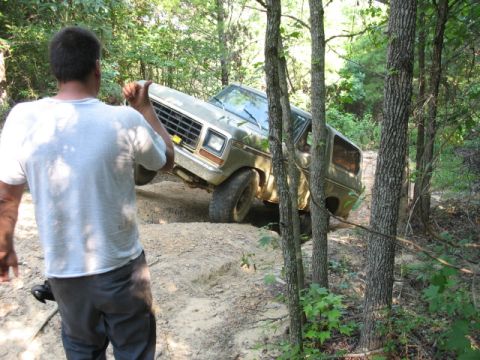1978 Ford Bronco - A man watches as a vintage Ford Bronco navigates a challenging off-road trail through a wooded area.
