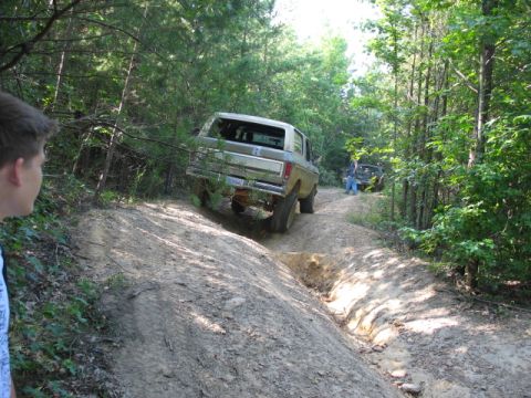 1978 Ford Bronco - A 1978 Ford Bronco navigates a rutted dirt path in a wooded area, with another vehicle visible in the background.