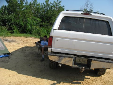 1978 Ford Bronco - A white SUV is parked on a dirt lot with a young boy sitting in a chair nearby.