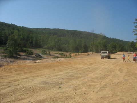 1978 Ford Bronco - Two trucks and several people are in a dirt area with trees and hills under a clear blue sky.