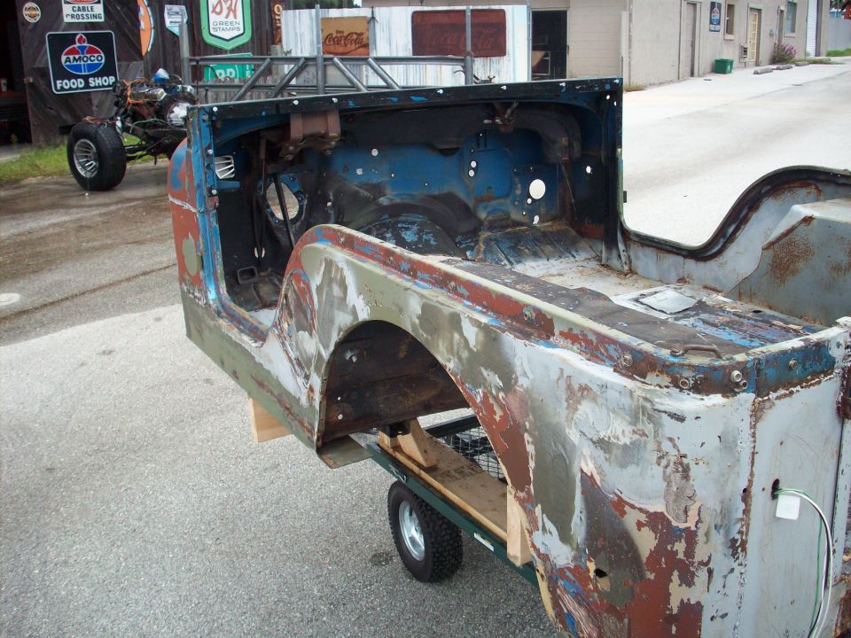 1978 Jeep CJ5 body on a dolly, showing rust and peeling paint, with a roll cage frame attached
