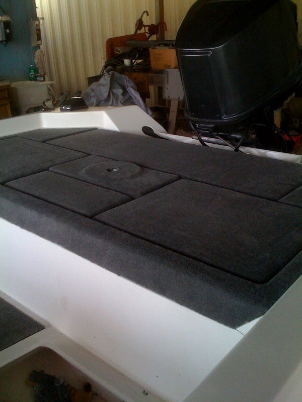 Boat deck with gray carpeted hatches and a black outboard motor in the background