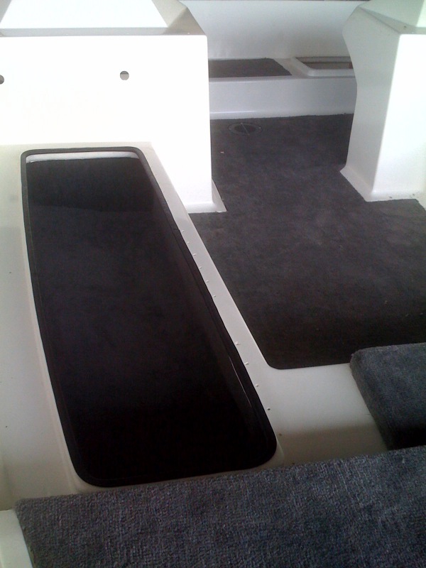 Interior of a boat with dark carpeted floor and white molded seating areas