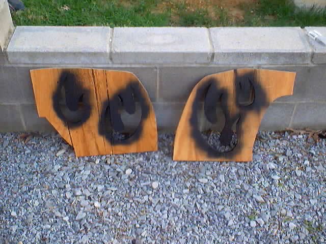 Two wooden cutouts with black spray paint, leaning against a concrete wall