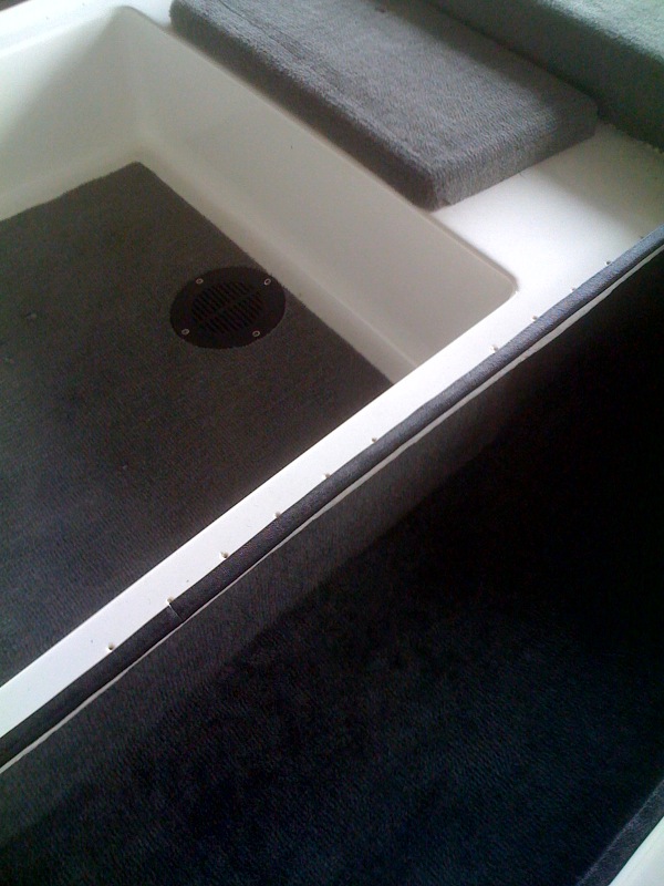 Carpeted fiberglass storage compartment with white walls and a round vent cover