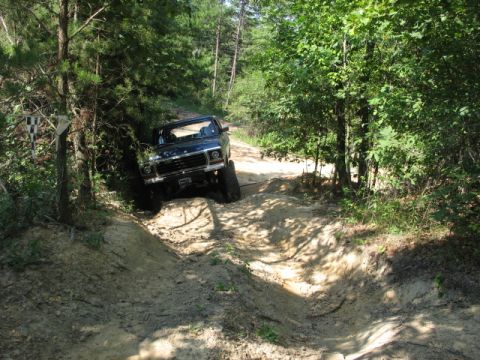 1978 Ford Bronco - 1978 Ford Bronco tackling an off-road trail through a wooded area.
