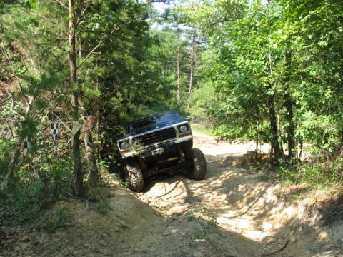 1978 Ford Bronco - A dark blue 1978 Ford Bronco navigates a challenging dirt trail with steep inclines and dense foliage.