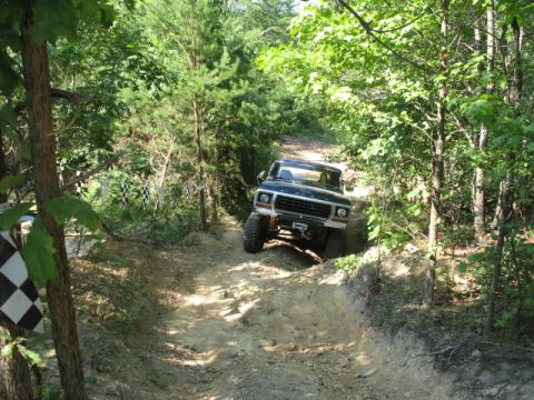 1978 Ford Bronco - 1978 Ford Bronco navigates a challenging off-road trail surrounded by dense forest.