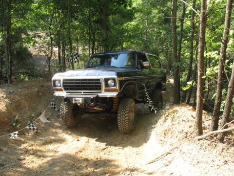 1978 Ford Bronco - A black 1978 Ford Bronco navigates a wooded off-road course with checkered flags visible.