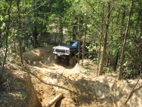 1978 Ford Bronco - A black 1978 Ford Bronco navigates a challenging dirt path through a wooded area, marked by checkered flags.