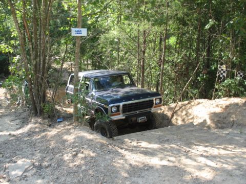 1978 Ford Bronco - A dark blue 1978 Ford Bronco tackles a challenging off-road course with a "LOG JAM" sign visible.