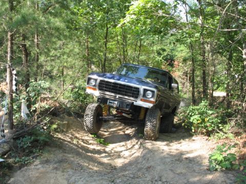 1978 Ford Bronco - A blue 1978 Ford Bronco navigates a challenging off-road trail through a wooded area.