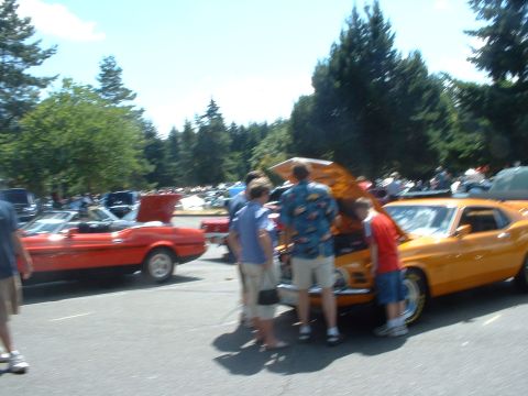 1999 Ford Crown Victoria - Orange 1970 Ford Mustang coupe with hood open at an outdoor car show.