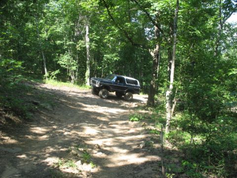 1978 Ford Bronco - Black 1978 Ford Bronco navigating a rocky, wooded trail.