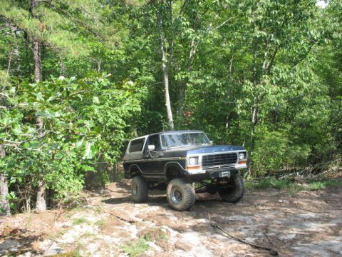 1978 Ford Bronco - A lifted 1978 Ford Bronco navigates a wooded trail with its front end angled towards the camera.