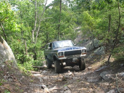 1978 Ford Bronco - 1978 Ford Bronco tackling a challenging rocky trail in a wooded area.
