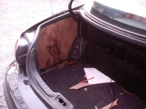 1999 Ford Taurus - The trunk of a 1999 Ford Taurus shows unfinished wood paneling on the left side and carpeted floor with some debris.