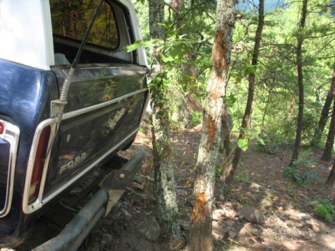 1978 Ford Bronco - The rear of a 1978 Ford Bronco is visible, parked on a dirt path surrounded by trees.