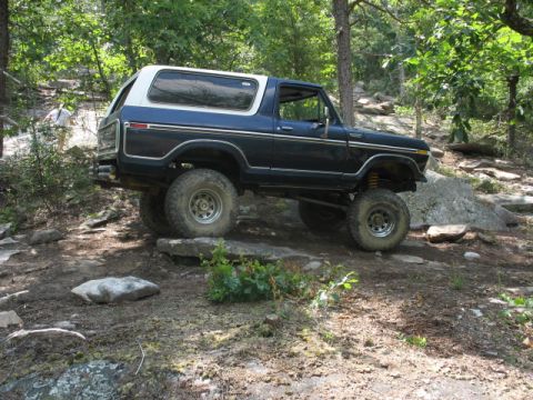 1978 Ford Bronco - A 1978 Ford Bronco navigates a challenging rocky trail in a wooded area.